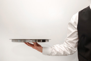 A waiter / butler in white shirt and black suit vest carrying an empty silver tray. Copy space on...