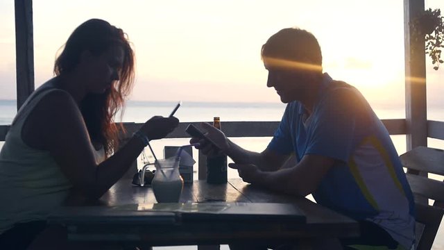 A man and a woman are sitting in a cafe by the sea, everyone is looking into their phone, not a beautiful sunset. slow motion. 1920x1080. full hd