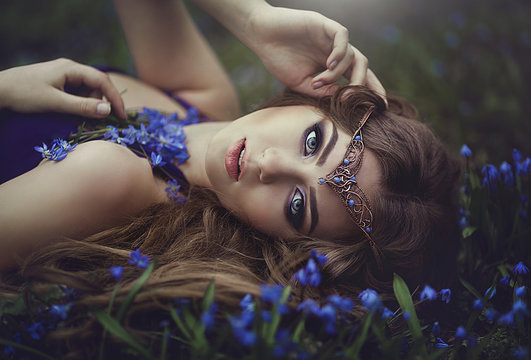 Elf girl with long hair and blue eyes in the tiara rests in spring forest blue forest flowers. Girl Princess dreams.