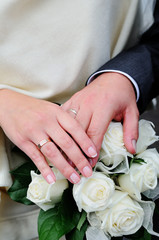 Obraz na płótnie Canvas Hands of newlyweds with wedding rings on a bouquet of the bride with white roses.