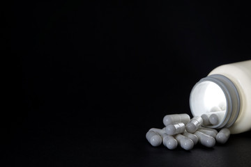 A can of magic pills. A white jar that glows with pills spilled on black background. Blank copy space for own text.