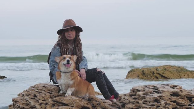 Young woman with corgi dog posing on the beach, girl with dreadlocks and hat with pet 