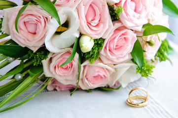 Gold wedding rings and a bouquet of the bride with pink roses.