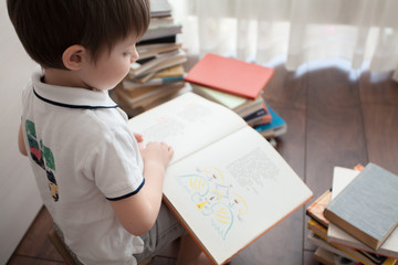  A cute baby is sitting and reading a large book.