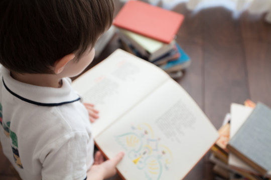  A cute baby is sitting and reading a large book.