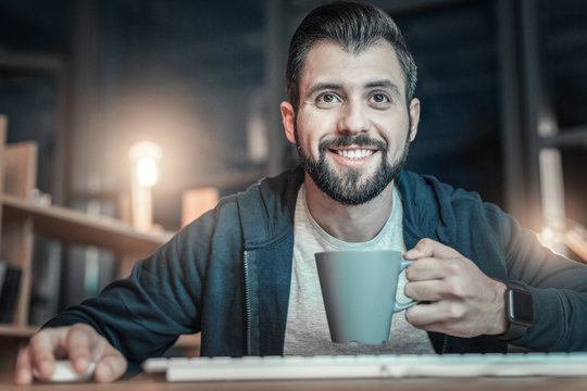 Visual Programming Language. Positive Cheerful IT Guy Rising Cup While Sipping Coffee And Using Mouse