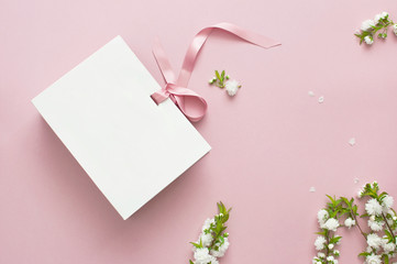 Flat lay top view White gift bag and spring flowers on a pink background. Greeting card with delicate flowers Pink floral background