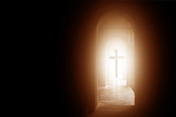 Silhouette of the cross at the end of tunnel with ray of sunlight behind