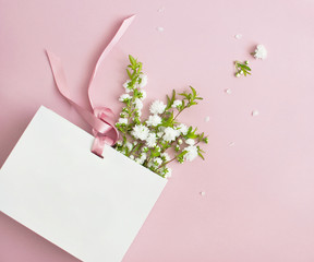 Flat lay top view White gift bag and spring flowers on a pink background. Greeting card with...