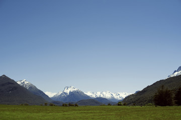 Paisaje minimalista de prado verde con montañas nevadas de fondo y cielo azul despejado	