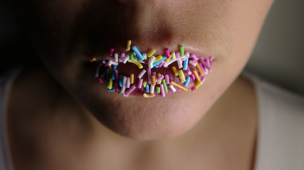 A woman's lips are covered of rainbow sprinkles / topping after eating an ice cream. Concept for eating sweets, sugar or being a sweet tooth.