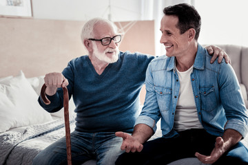 Time together. Happy nice young man smiling and talking while spending time with his father