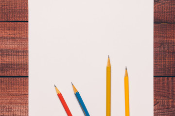 Bright used colorful pencils next to a blank sheet of paper. Work supplies stationery on a wooden texture table. Trendy minimalism. Concept of a modern freelancer workplace. Rustic cozy atmosphere