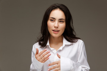 Beautiful girl in a white shirt shows emotions - thoughtfulness. On a light background.