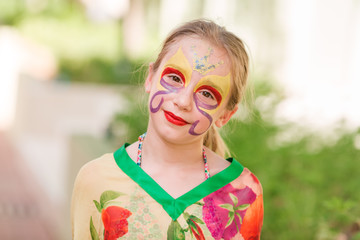 Happy little girl with face art paint in the park.
