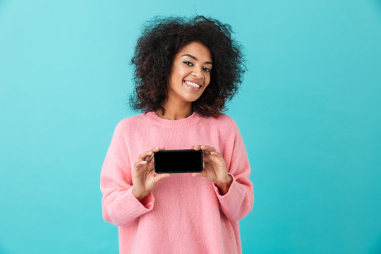 Portrait of cheerful woman 20s holding cell phone and demonstrating copyspace black screen, isolated over blue background