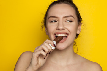 young happy woman enjoying eating chocolate on a yellow background