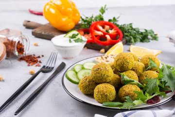 Homemade spicy chickpea falafel garnished with fresh vegetable and yogurt on a plate over light concrete background. Israeli cuisine concept