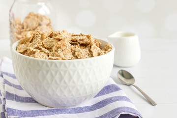 Whole wheat corn flakes  in white bowl on kitchen table, white background, front view.