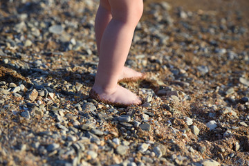 The legs of a small child. The legs of the child go along a sandy beach with pebbles to the sea