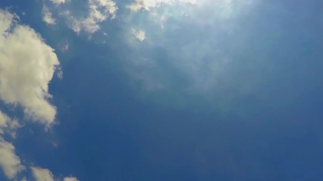 This is footage of small clouds getting away from each other and floating onwards, while the sun is on top, shining very bright. Slow time-lapse, white clouds moving in a blue sky.