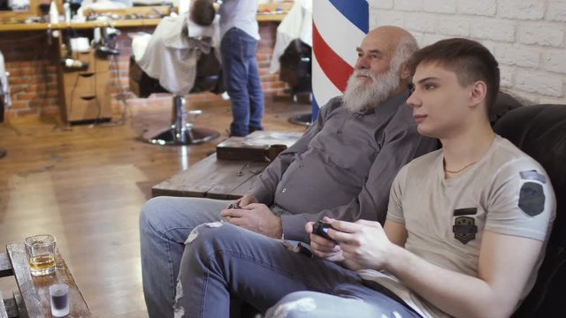 Young guy with mature man plays videogame in barbershop