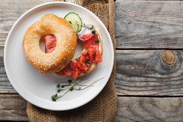 Bagels with salmon fish, cream cheese, cucumber and fresh radish slices on rustic gray wooden background