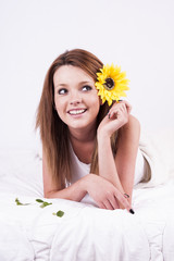 Beautiful young woman with sunflower lying in bed