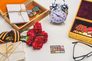 closeup shot of alarm clock, eyeglasses, flowers wrapped by st. george ribbon, letters, medals on gray, victory day concept