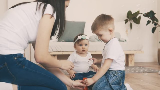 Little son in jeans and white t-shirt try to make bubbles in the room with young mother. Happy family concept
