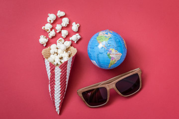 High angle view of cone with popcorn and movie theater eyeglasses with globe model on red...