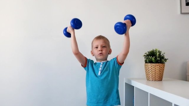 Smiling boy is doing exercises with dumbbells in his room