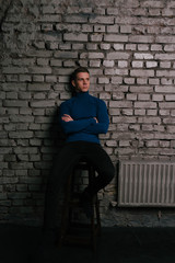 Fototapeta na wymiar white attractive guy sits on a brick wall background dressed in a blue sweater and black pants