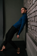 white attractive guy is nearby a brick wall background dressed in a blue sweater and black pants