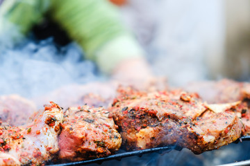Man is cooking BBQ Roasted Pork Meat With herb spice On The Hot Charcoal Grill With Smoke.