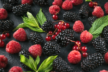 Macro photo of ripe berries of blackberry, raspberry and currant and green mint leaves on a black surface.