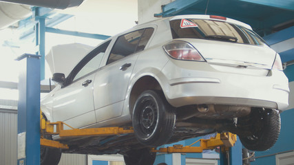 Car in auto service lifting for repairing, mechanics in garage