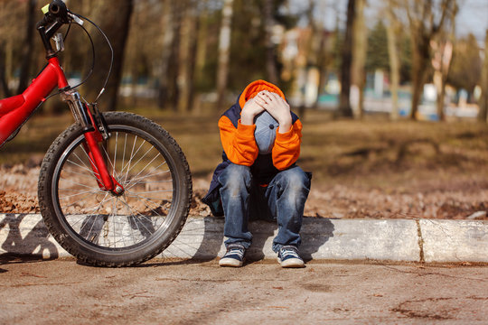 Sad child sitting near a broken bicycle
