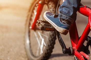 Detail of child cyclist feet riding bike on outdoor in sunny road. Closeup on pedal and foot
