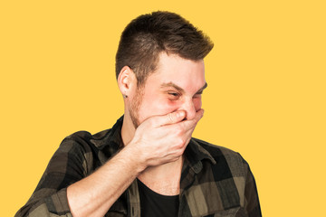 Fototapeta premium Young guy with beard and modern hairstyle mohawk, laughs and closing his mouth with his hand, isolated on yellow background.