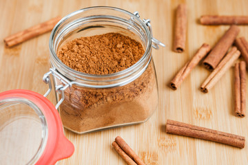 Glass jar with cinnamon powder and several cinnamon sticks close-up
