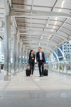 business man and business woman wear black suit walk together with luggage on the public street, business travel concept