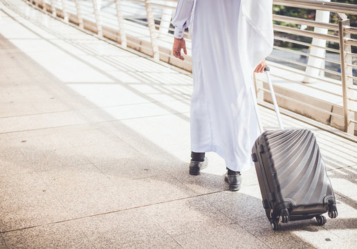 Muslim man wear white coat walking  on public street with black luggage. business travel concept.