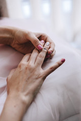 Hands of the bride with beautiful gentle manicure, touches an engagement ring on a finger with a diamond close-up. In a pink wedding dress
