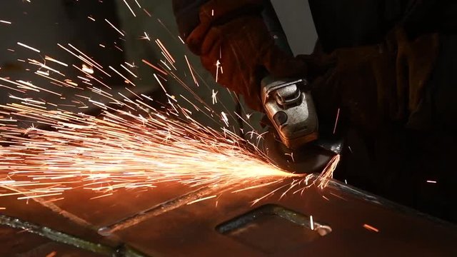 worker grinding weld seam with grinder machine and sparks. Slow motion