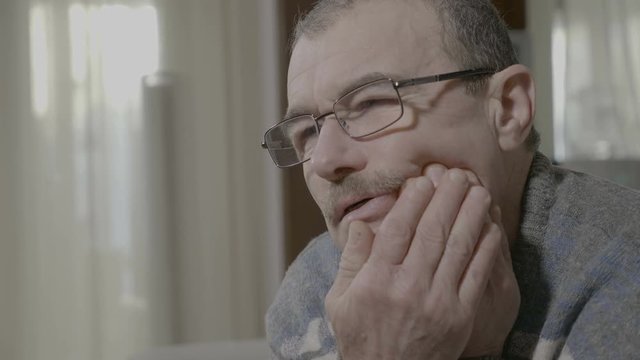 Senior man suffering from strong tooth pain rubbing his cheeck feeling bad