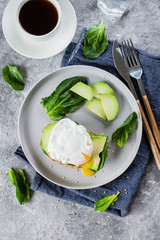 Sandwich with avocado, spinach and poached egg on whole wheat bread on plate on stone background. Helathy Food Breakfast Concept. Top view