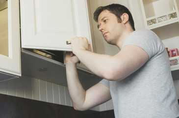 Professional handyman installing cabinet door in the kitchen.