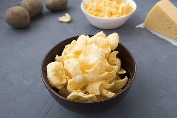 Potato chips with cheese in a plate that is located on a gray background.