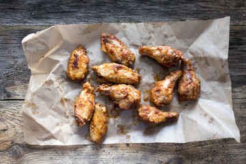 Appetizing fried pieces of chicken, pieces of chicken wings located on paper and on an old wooden background.